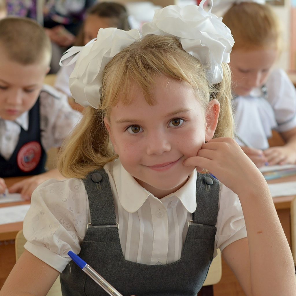 Pédagogie de Chkola, image petite écolière blonde avec deux couettes qui sourit le stylo à la main
